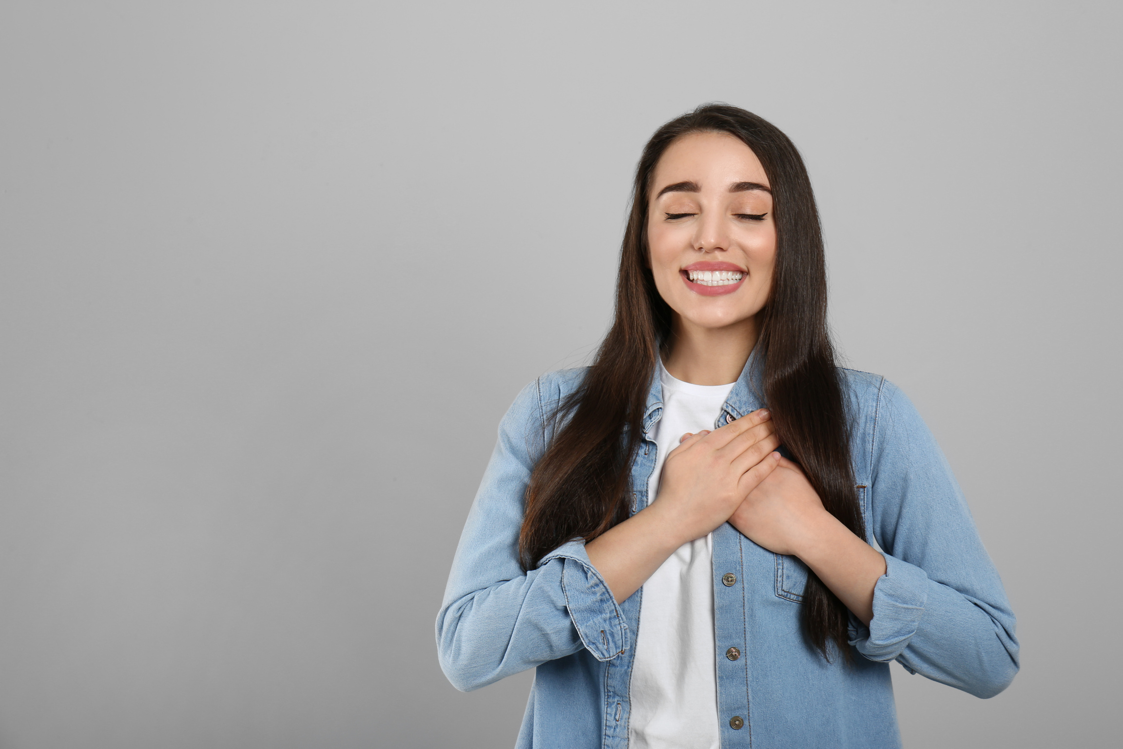 Beautiful Grateful Woman with Hands on Chest against Light Grey